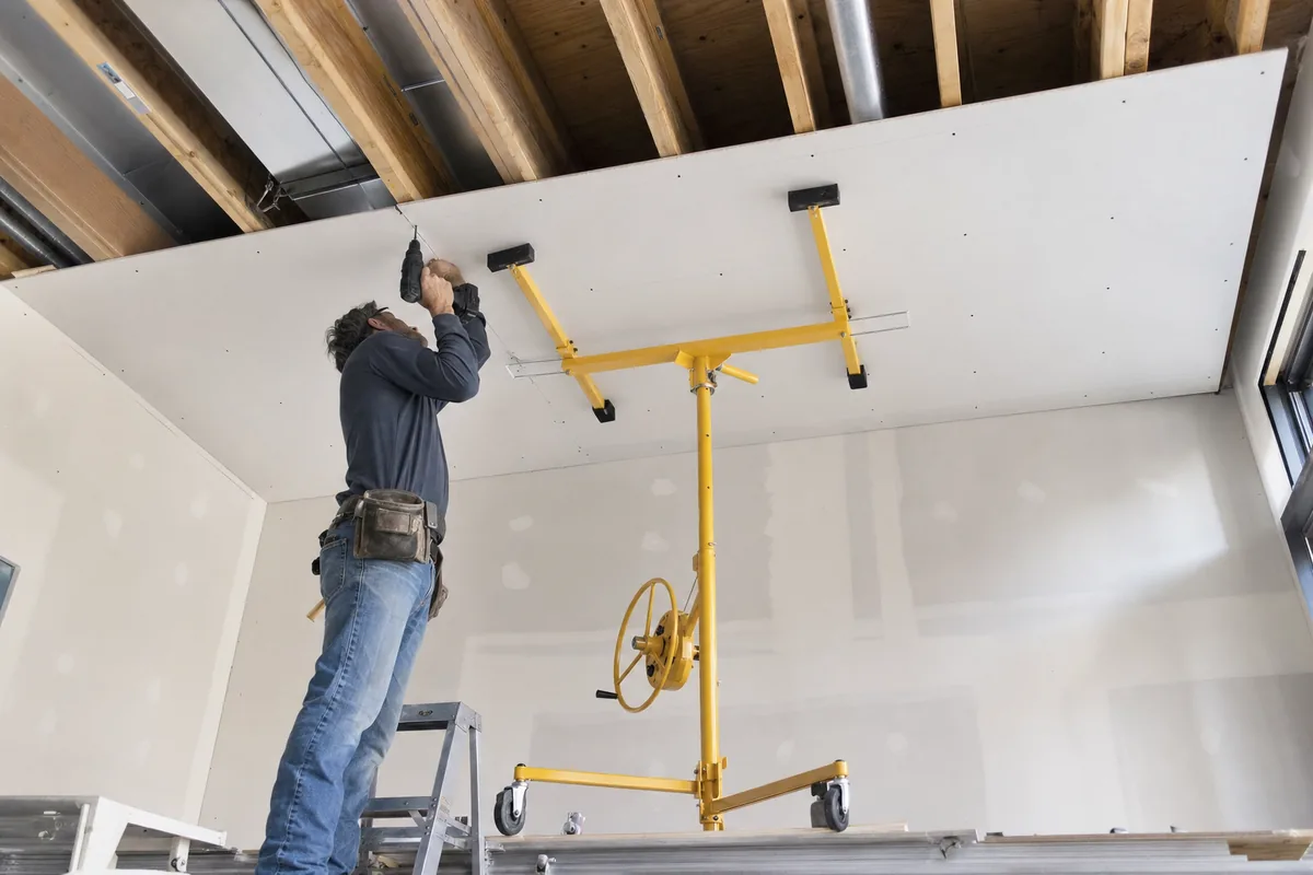 Drywall panel being fixed to ceiling joists with a panel lift